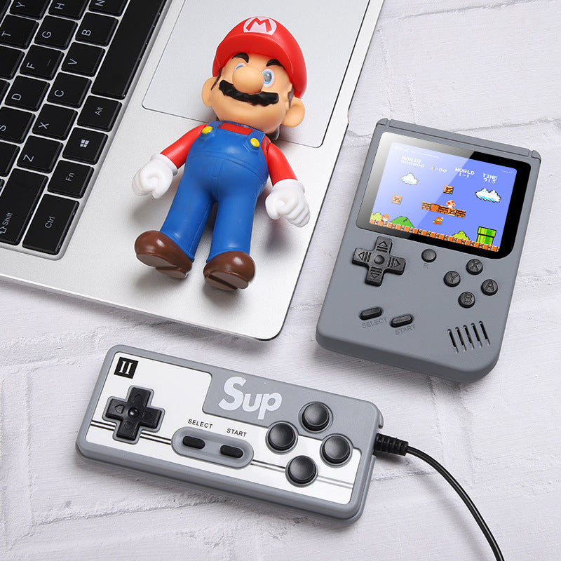Super Mario figurine next to a handheld gaming console and controller on a light surface.