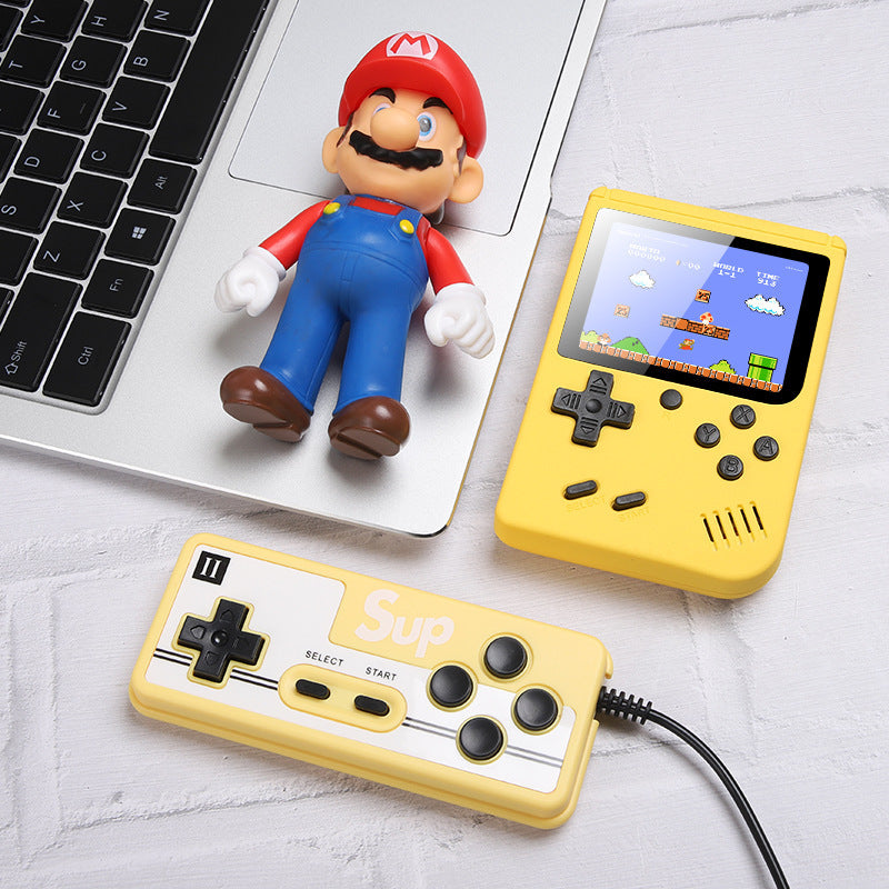 Handheld game console with Mario figurine and laptop on a light gray surface