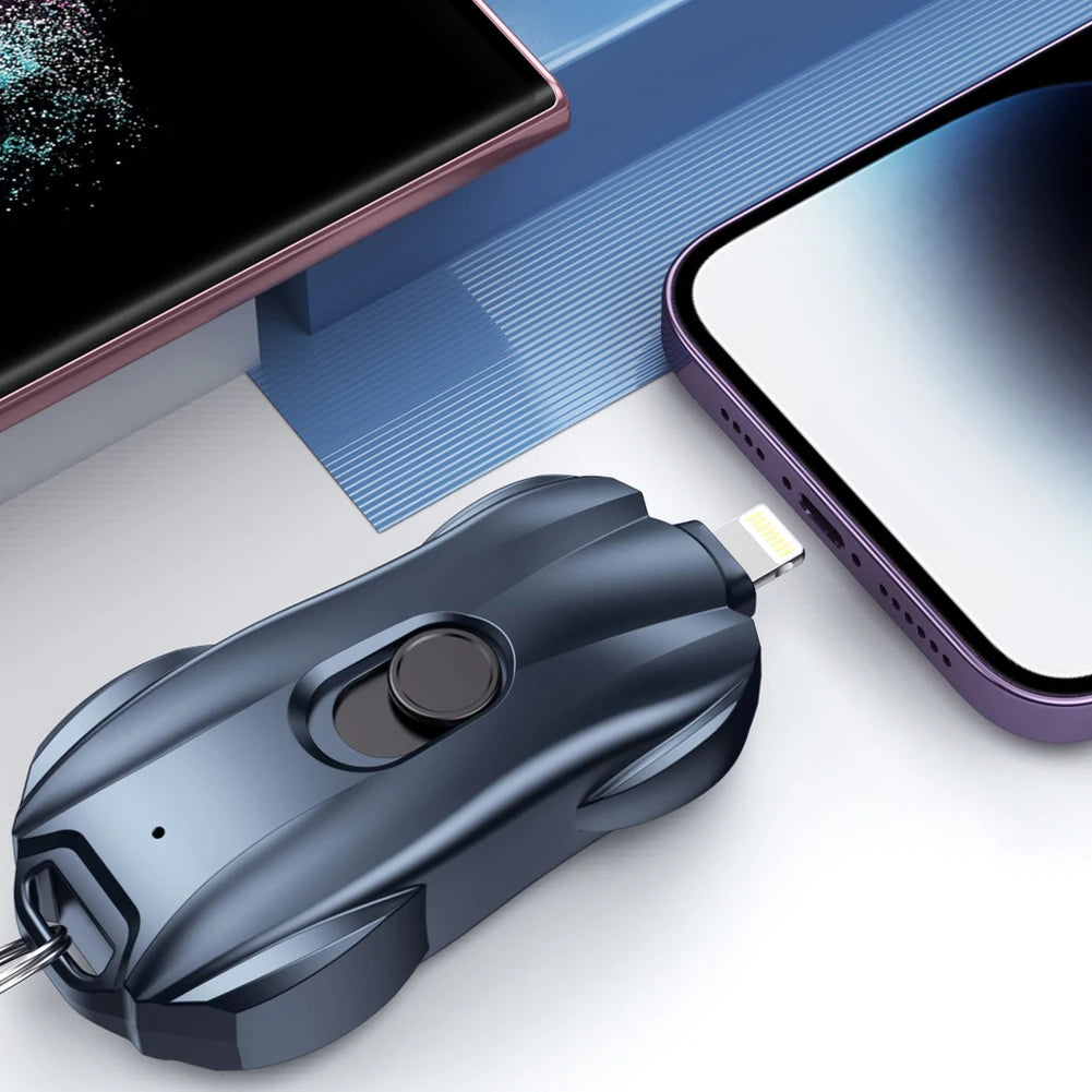 Black wireless car shaped powerbank with keychain attachment on a white surface with smartphone and blue box in the background
